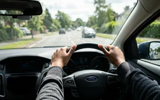 A learner's hands on the steering wheel on a quiet road